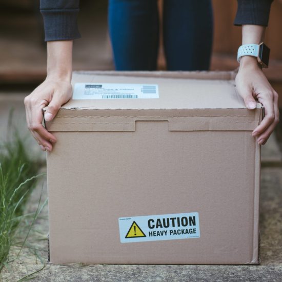 A person resting his arms on a cardboard box with a label "caution heavy package " on it